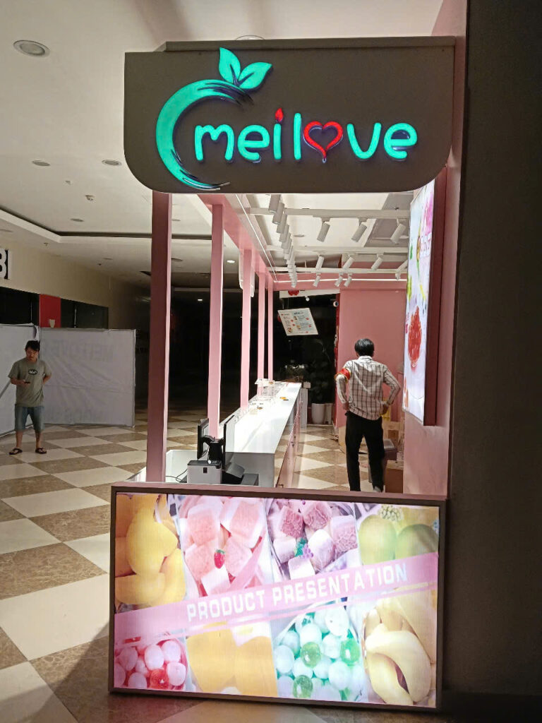 Chính diện đầu quầy MELOVE với biển logo phát sáng và màn hình bánh kẹo trong lúc hoàn thiện