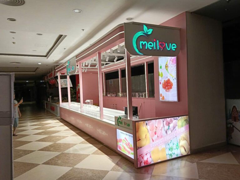 Đầu quầy MELOVE có logo phát sáng và màn hình sản phẩm nhìn từ hành lang trung tâm thương mại